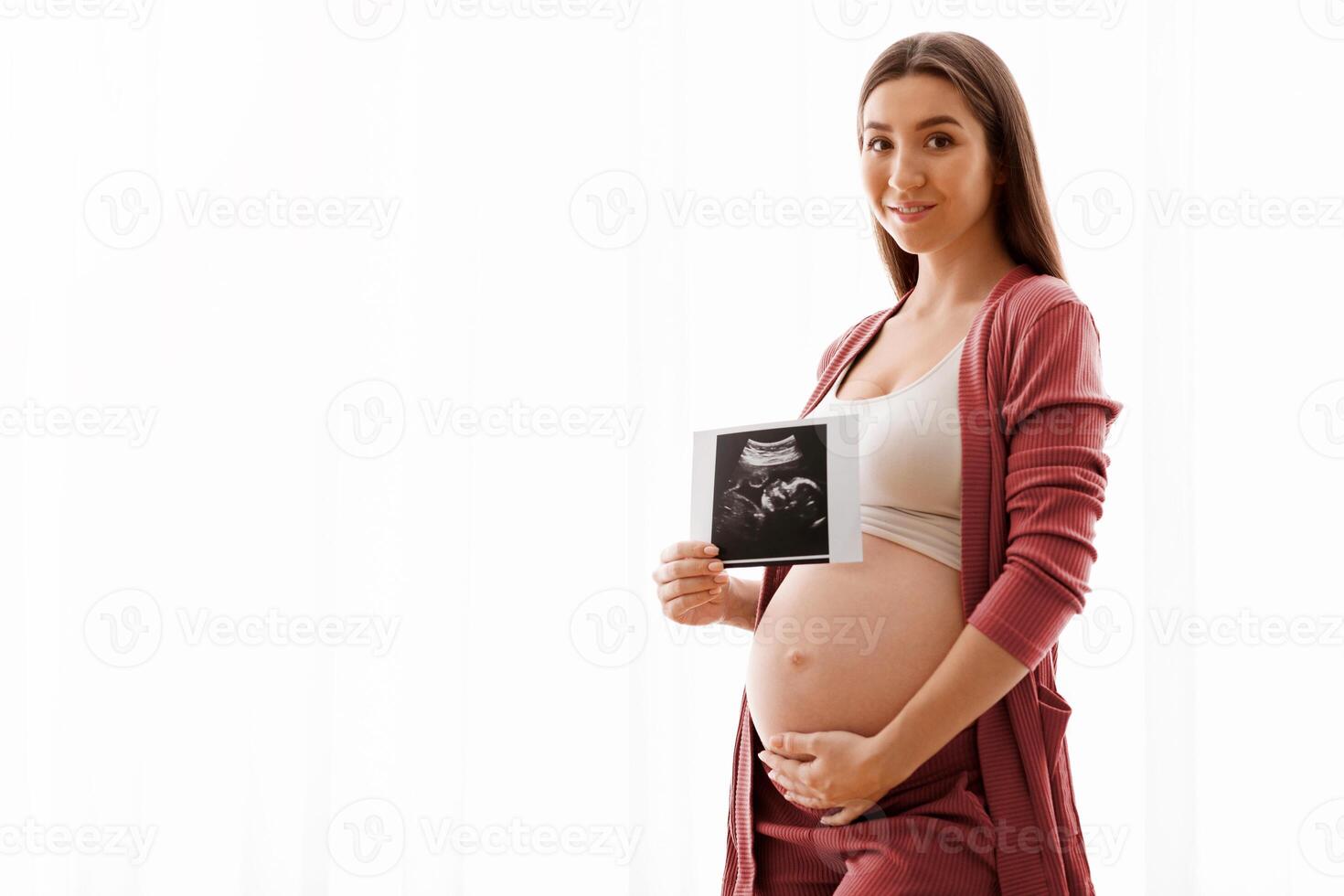 Cute Pregnant Lady Posing With Baby Sonography Photo Near Window At Home, Beautiful Expectant Lady Tenderly Touching Her Belly And Smiling At Camera, Enjoying Healthy Pregnancy And Future Maternity