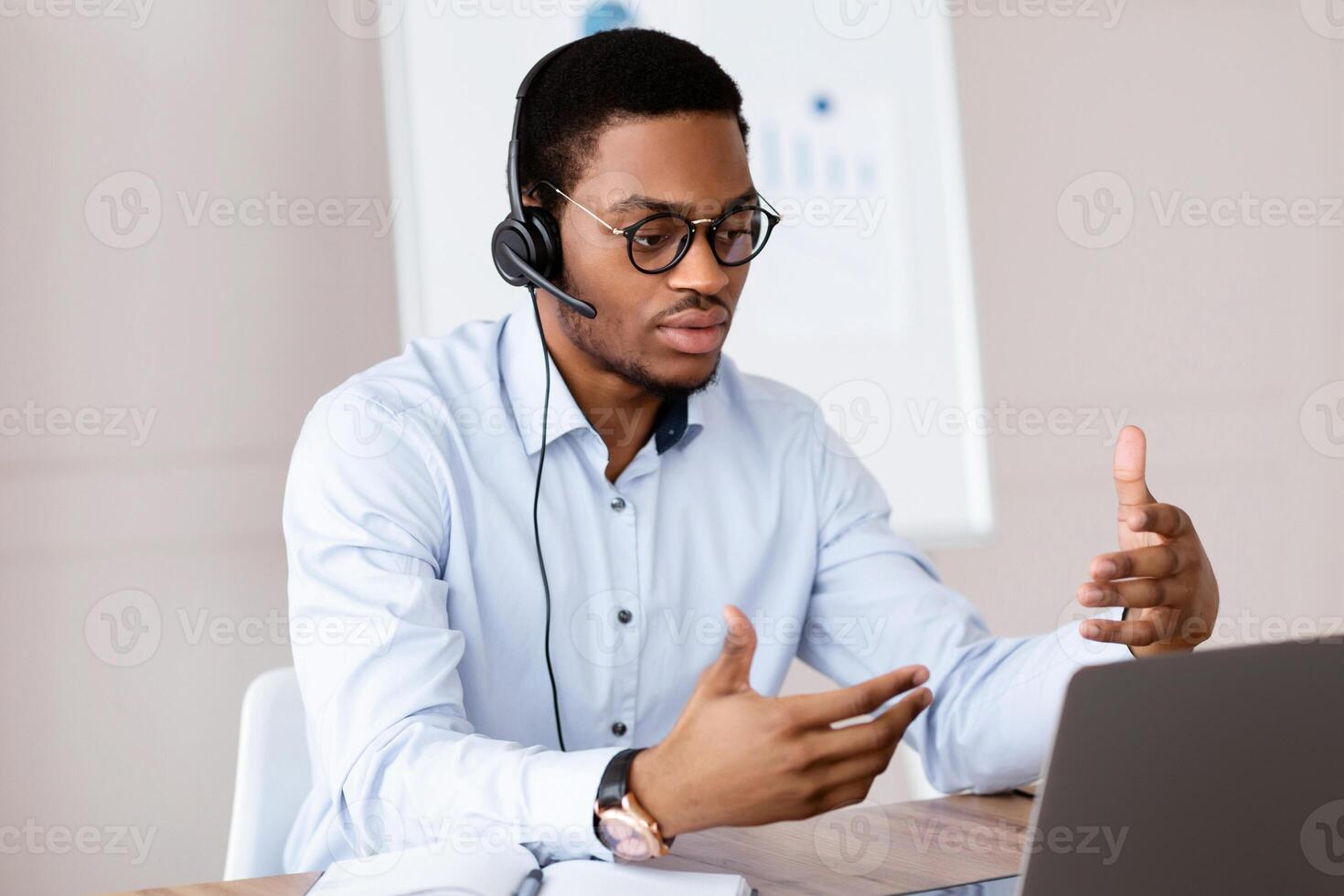 African american man having call with cleints or business partners via laptop, office interior, copy space. Handsome black manager or business coach broadcasting from his working place photo