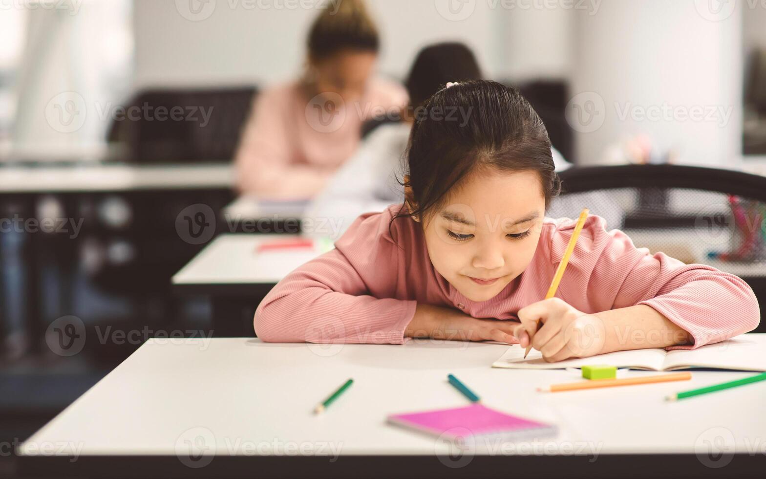 Tuition Concept. Portrait of concentrated small asian girl sitting at table in classroom, writing or drawing in notebook, doing homework or taking notes during lesson, selective focus, free copy space photo
