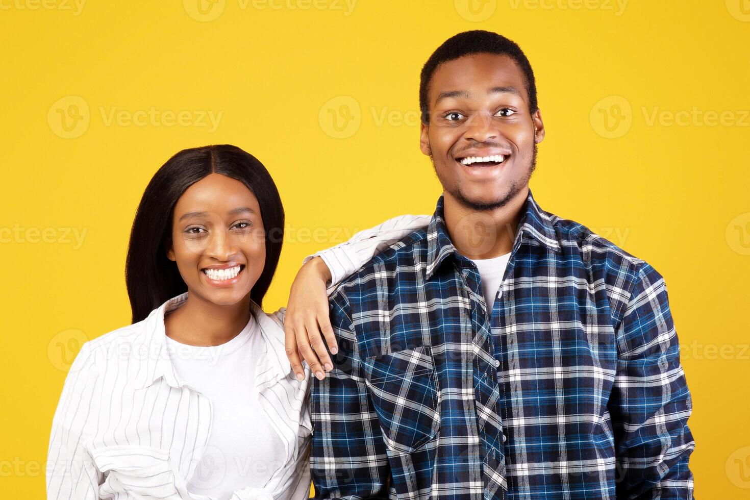 Happy human emotions. Smiling millennial african american couple in love in casual, look into camera, lady puts her hand on male shoulder, isolated on yellow background, studio shot, copy space photo