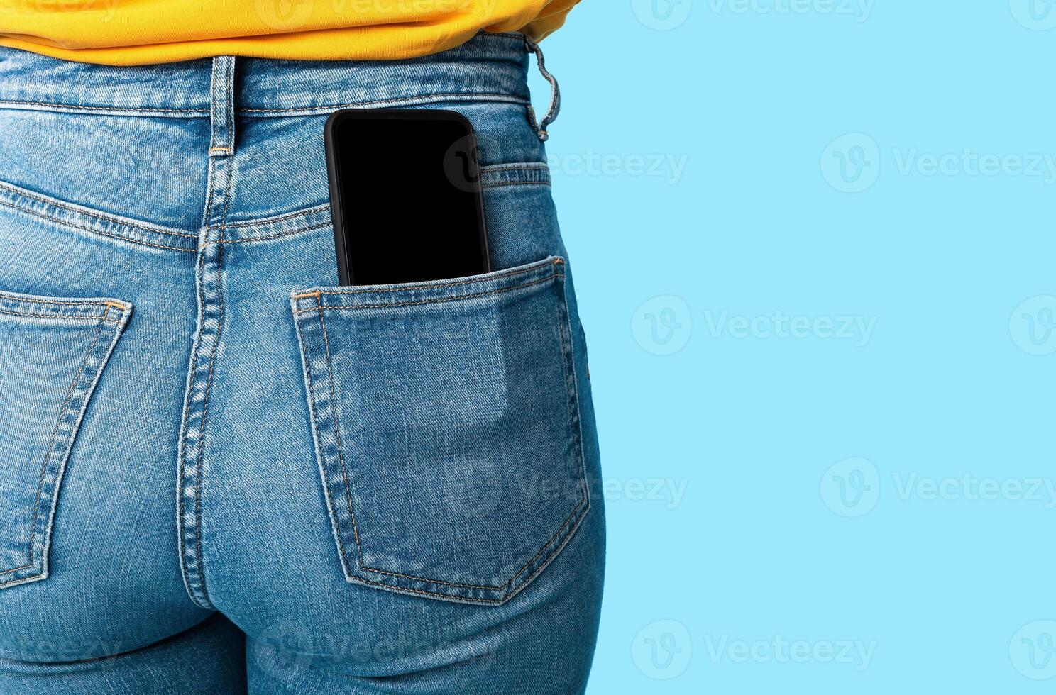 Cropped view of female having cellphone with blank screen in jeans pocket on blue studio background, mockup for mobile app or website. Free space for your advertisement template photo