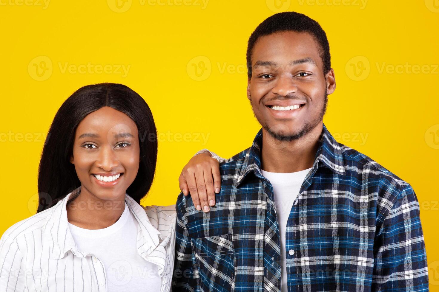 Family portrait, couple in love and fun together. Millennial smiling african american lady in casual put her hand on husbands shoulder and looking at camera, isolated on yellow background, empty space photo