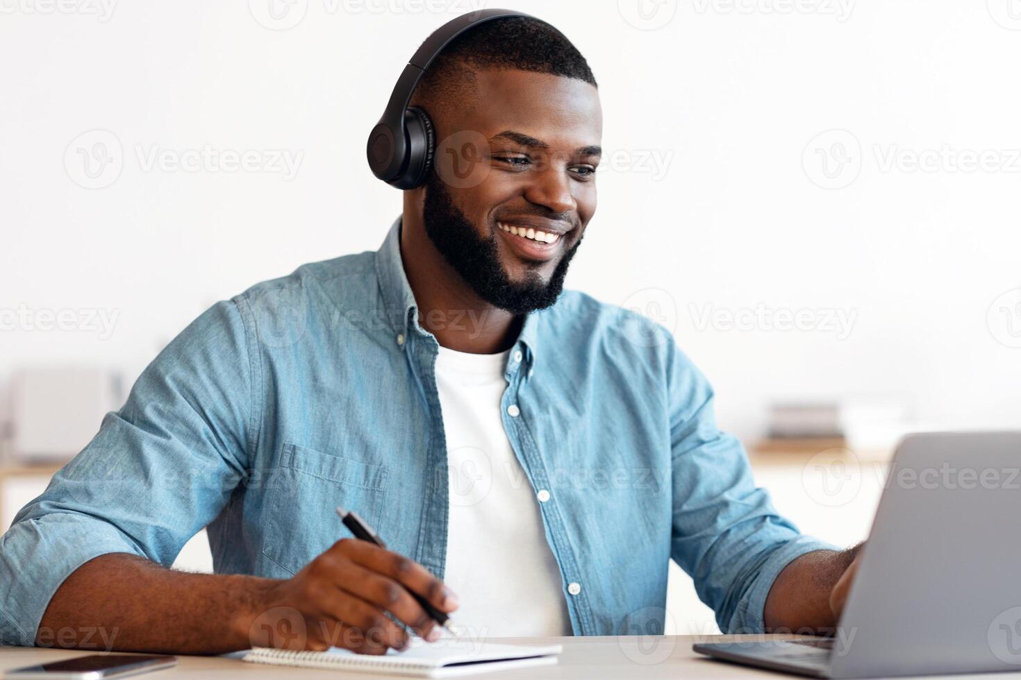 Online Education. Smiling Black Guy In Headphones Study With Laptop And Taking Notes, Cheerful Millennial African American Man Using Computer And Writing Down Information, Enjoying Distance Learning photo