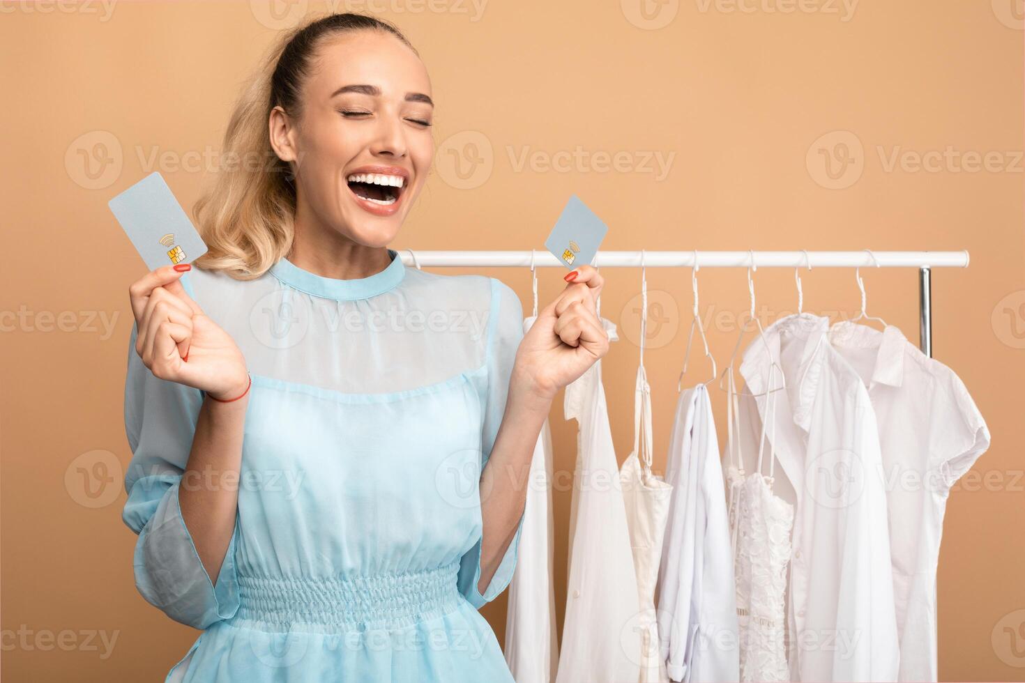 Time For Shopping Concept. Portrait of excited young woman holding and showing two debit credit cards, standing in wardrobe near clothing rail and screaming yes with joy, happy about purchases photo
