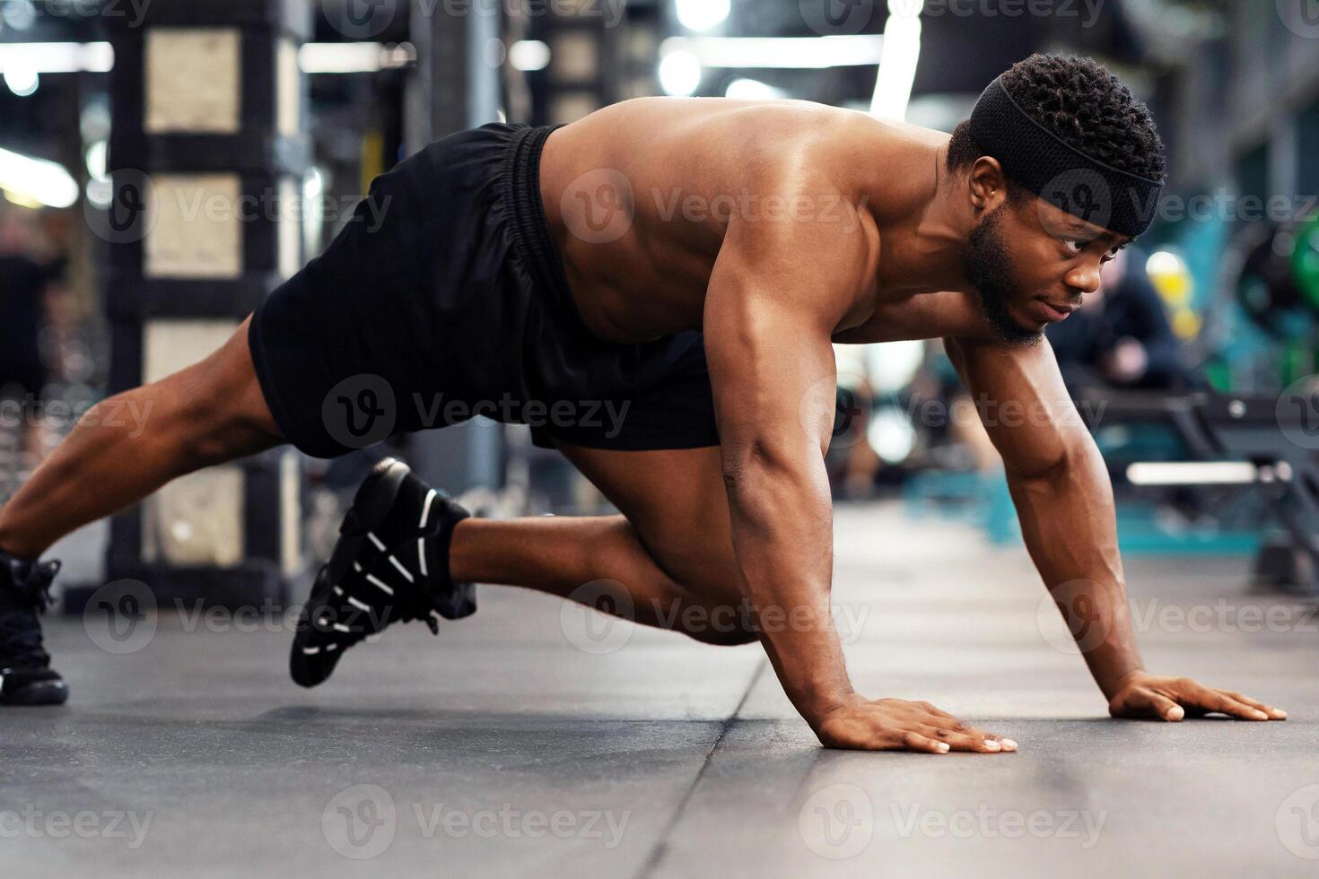 Plank work out concept. Active shirtless black man making work out on floor in modern male gym, side view. Motivated african american muscular guy bodybuilder planking knee to elbow, panorama photo