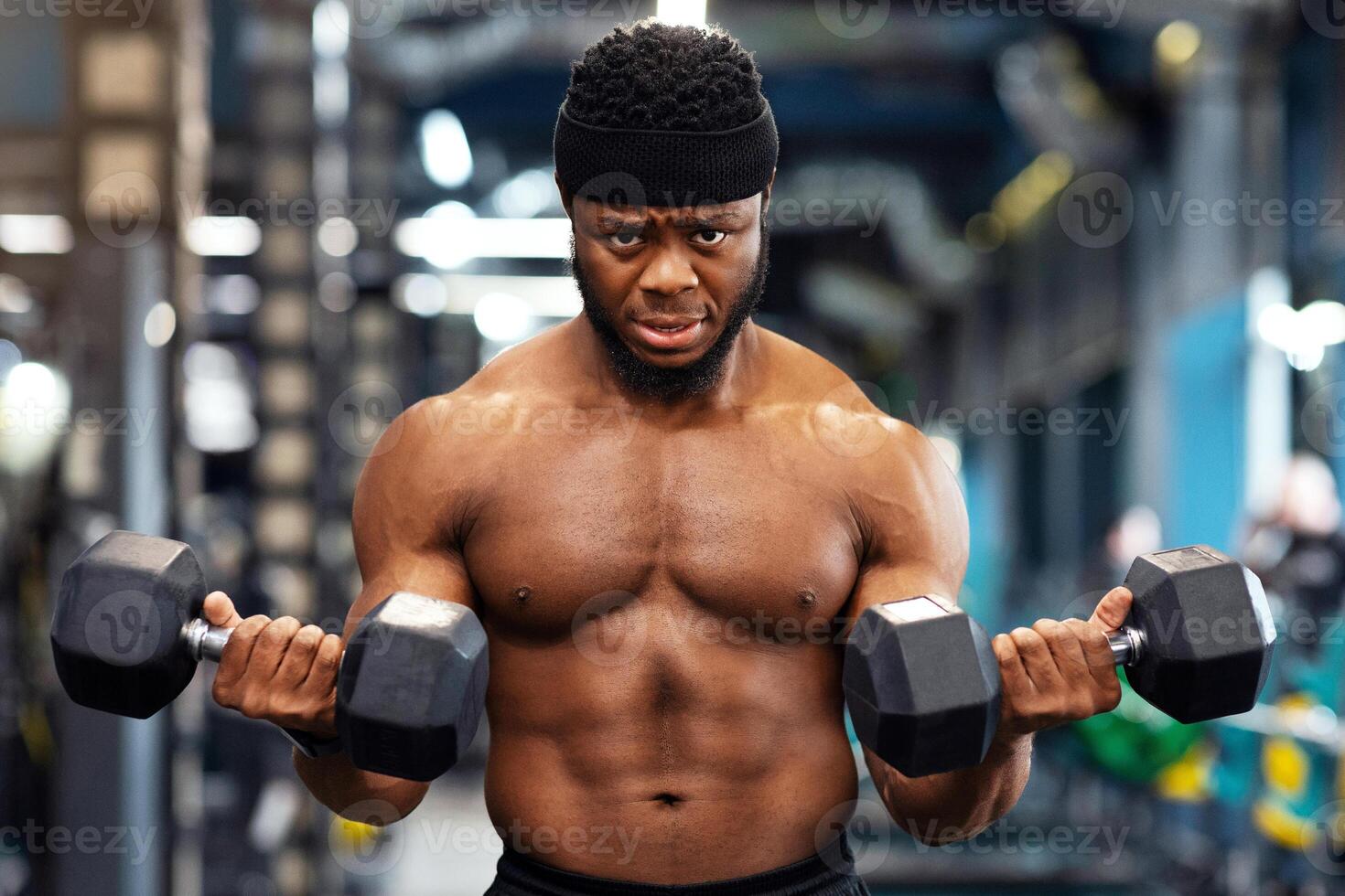 Muscular black guy doing workout with dumbbells at gym, lifting weight with both hands, copy space. Motivated african american man bodybuilder working on biceps, weight exercises concept photo