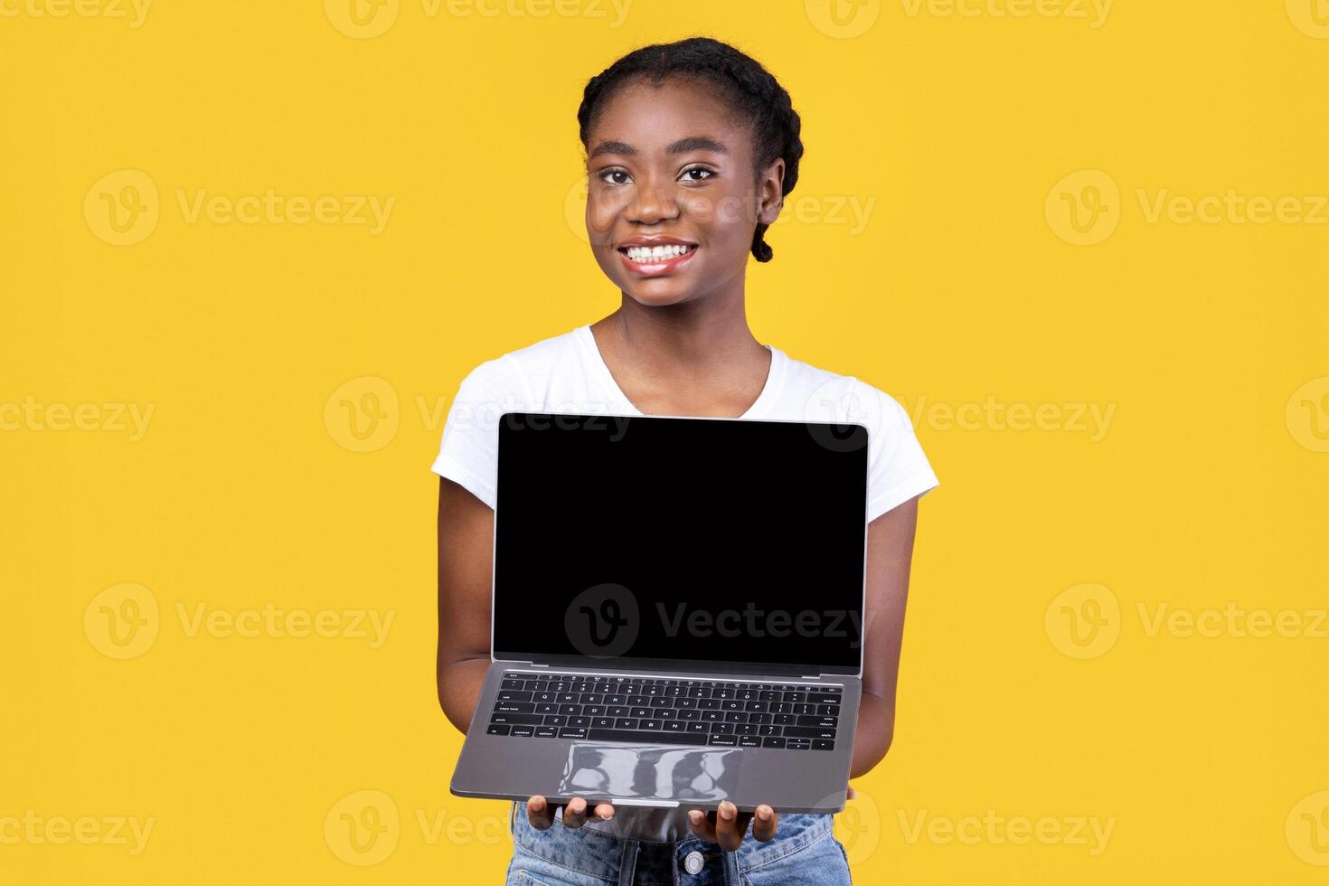 Cheerful Black Lady Showing Laptop Blank Screen Holding Computer Standing Posing On Yellow Studio Background, Smiling To Camera. African Woman Recommending Website. Mockup photo
