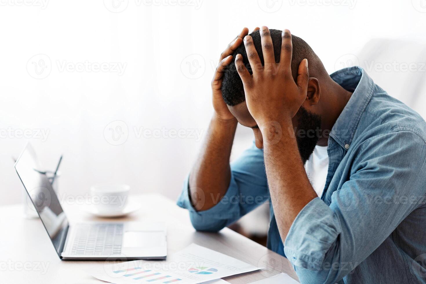 Stressed Black Entrepreneur Sitting At Desk And Looking At Financial Papers, Depressed African American Businessman Keeping Head In Hands In Despair, Having Troubles At Work, Copy Space photo