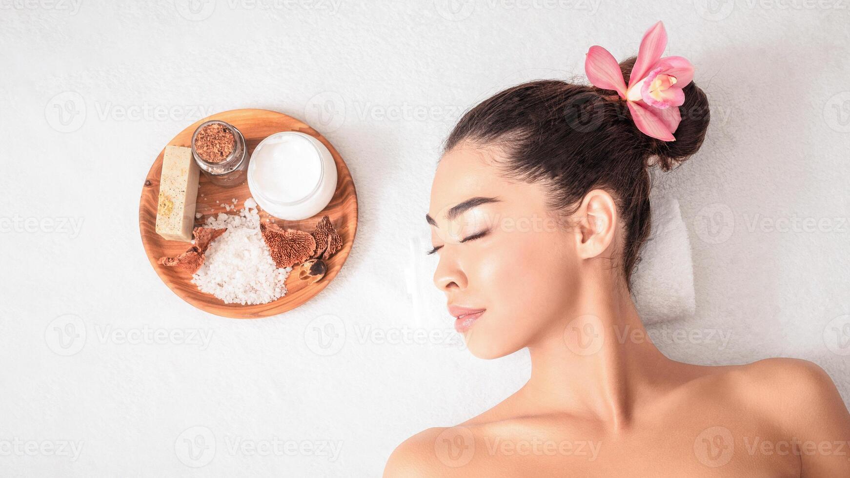 Asian Woman Relaxing During Aromatherapy Session With Natural Cosmetics In Beauty Spa, Lying On Massage Table With Closed Eyes, Enjoying Body Care And Self-Pampering, Top View With Free Space photo