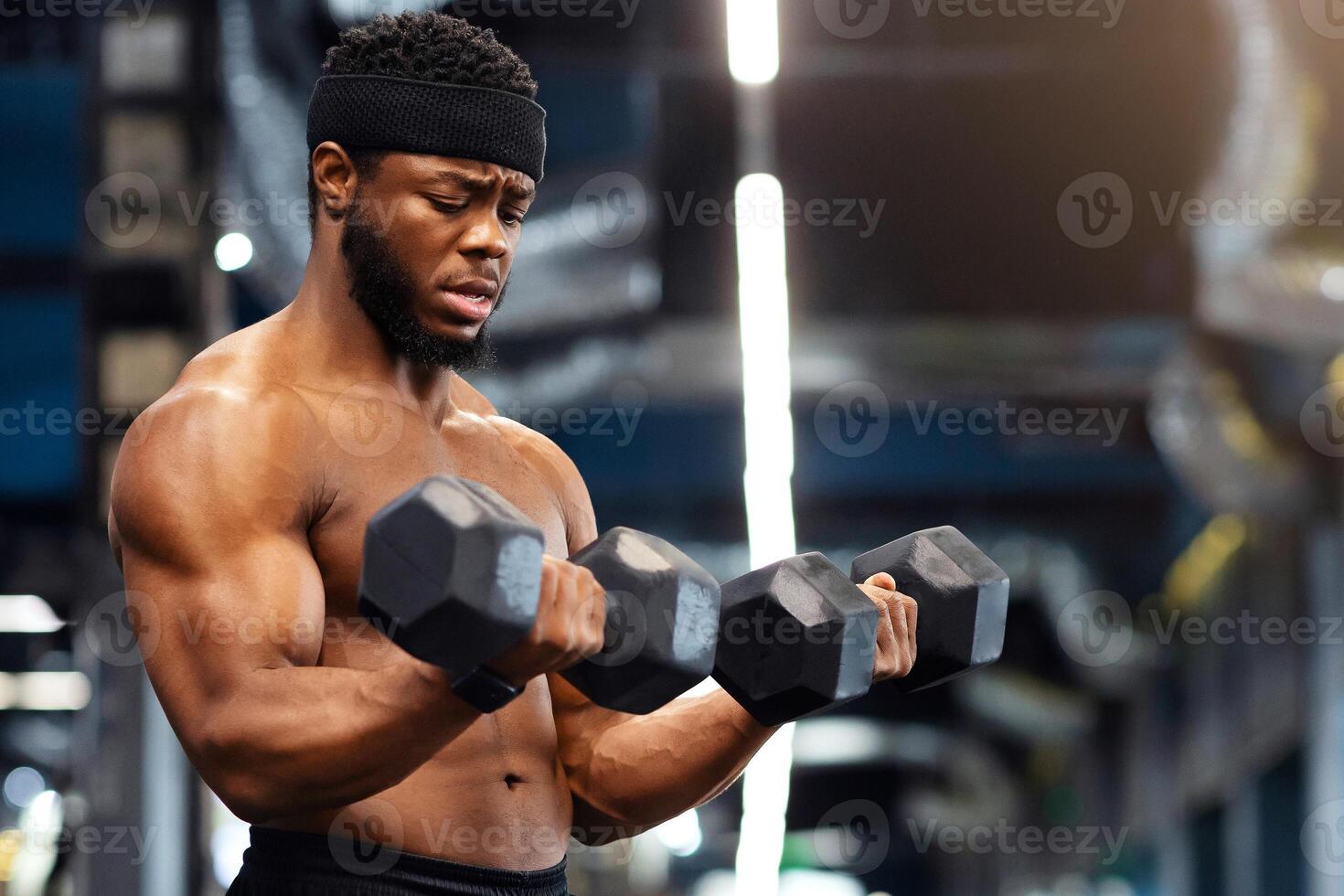 Handsome african american shirtless bodybuilder making work out with barbells at gym, copy space. Hot black guy exercising with two dumbbells, working on his muscular biceps photo