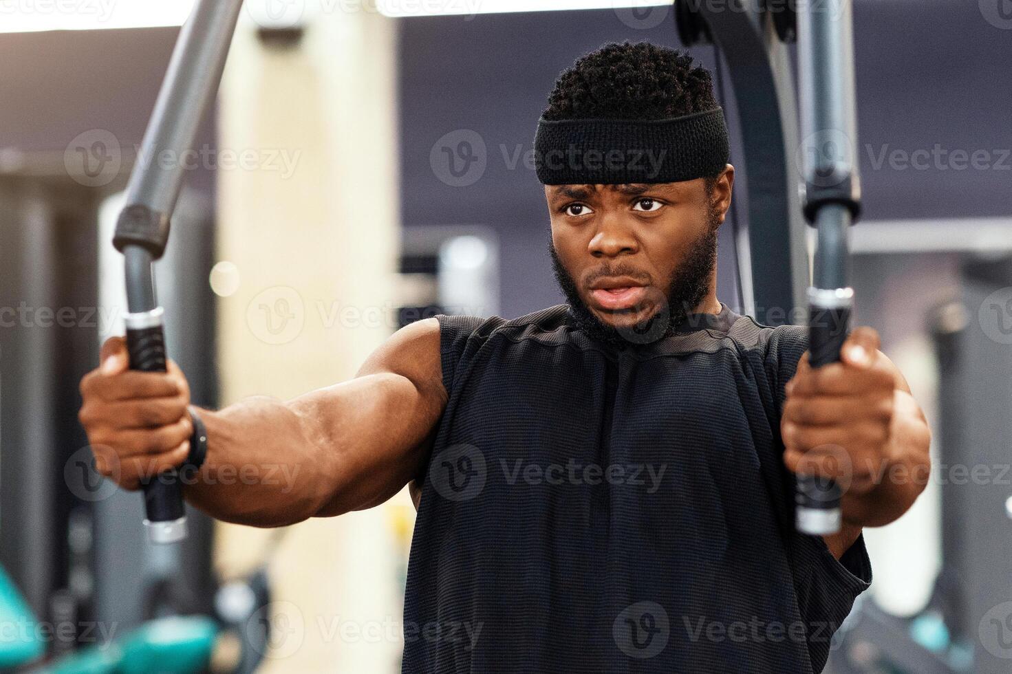 Young black sportsman training shoulders muscles and chest on block exerciser in gym, copy space. Motivated african american bodybuilder having workout at modern gym, using peck deck machine photo