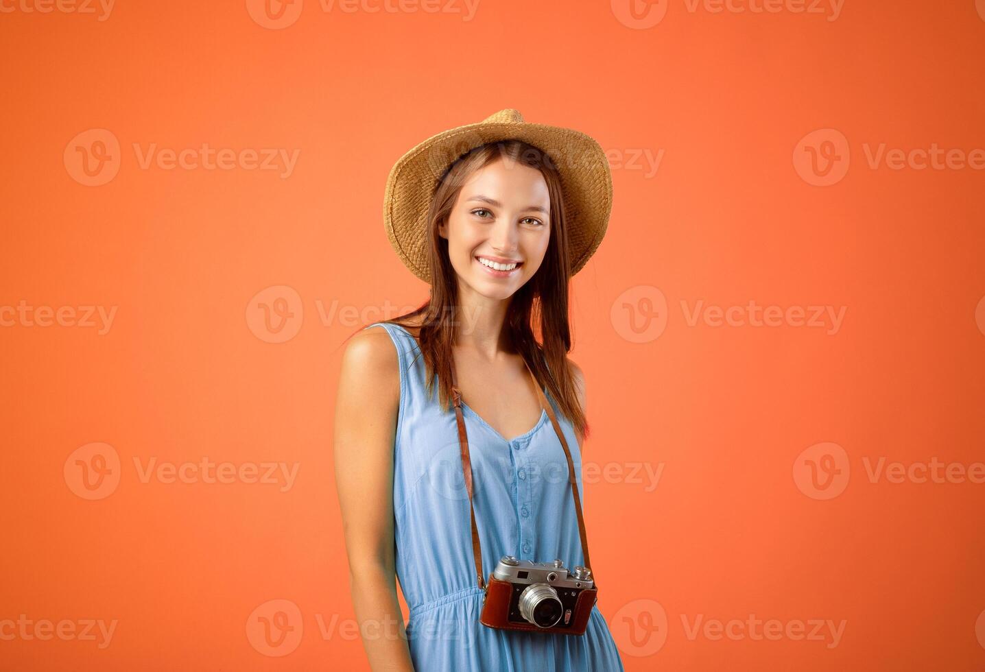 Going vacation. Happy woman tourist with camera and summer hat posing over yellow studio background, copy space. Young excited lady photographer getting ready before travelling, smiling at camera photo