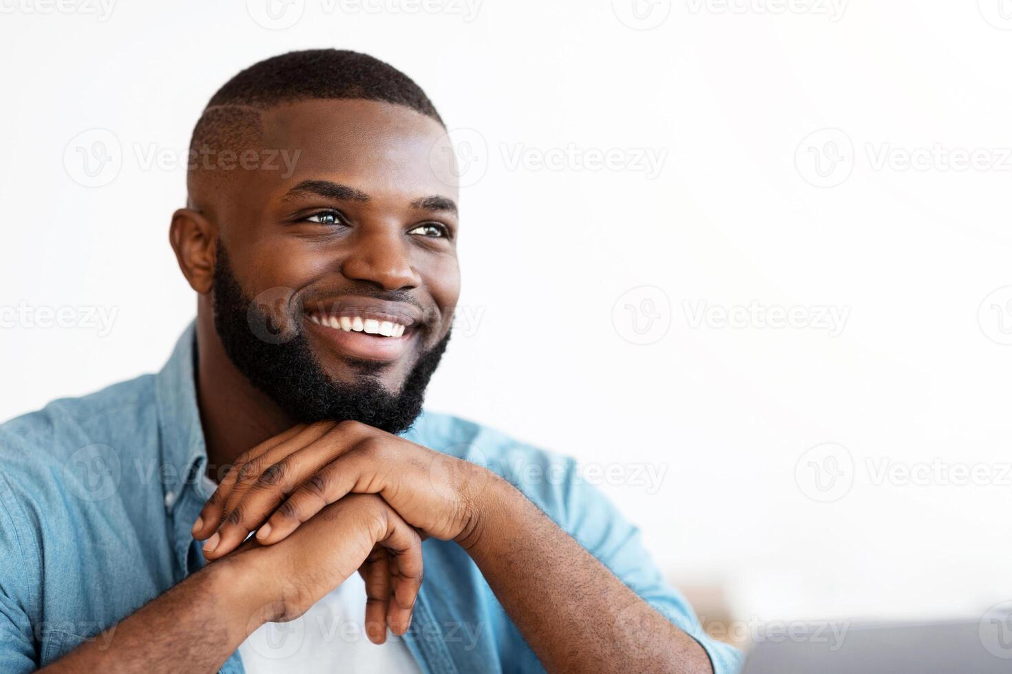 Portrait of cheerful successful African American freelancer guy sitting at desk with laptop and looking aside with pleased face expression. Black millennial man enjoying remote work, closeup shot photo