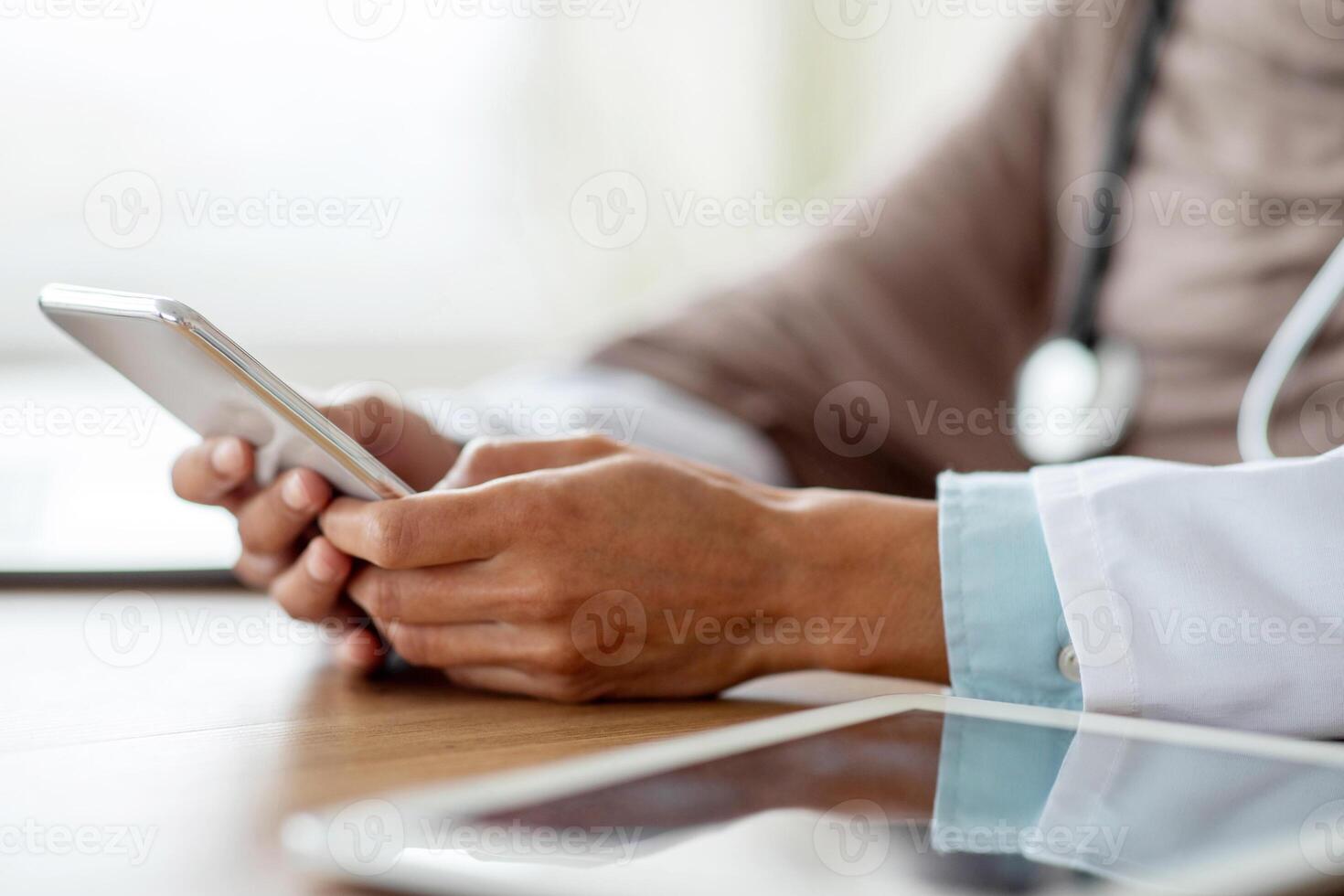 Cropped of female doctor using gadgets at workplace, holding smartphone and digital tablet. Unrecognizable therapist having online conversation with her patients, using mobile phone, closeup photo