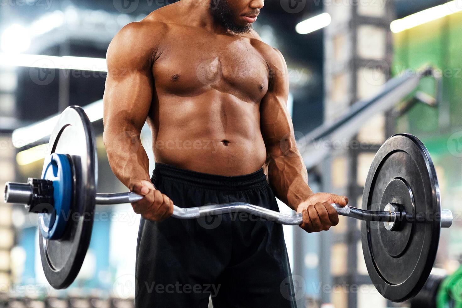 Athletic black guy making weightlifting or powerlifting, working on arms and chest musculs, copy space. Muscular african american man bodybuilder exercising with heavy barbell at modern gym photo