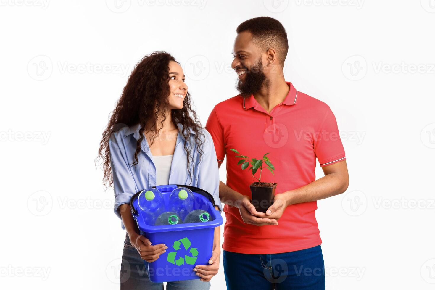 Care For Nature. Cheerful Diverse Couple Holding Plant And Bucket With Recycling Waste And Plastic Bottles Smiling Each Other Standing Over White Background. Clean Environment Concept photo