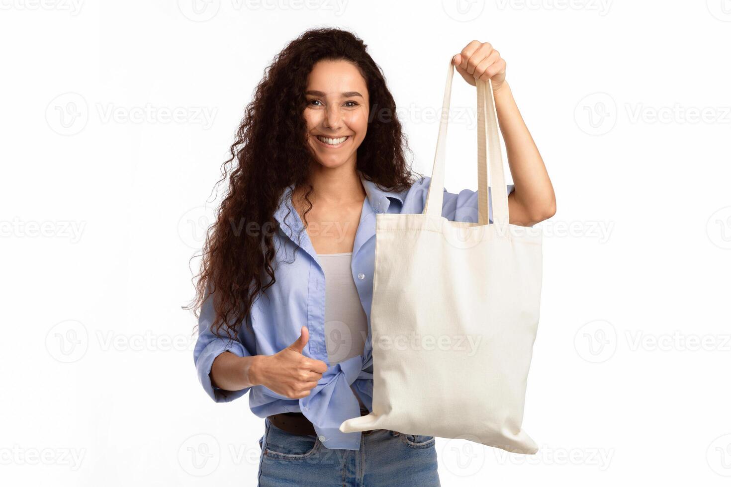Lady Showing White Eco Cotton Shopper Bag Gesturing Thumbs-Up Smiling To Camera Standing On White Studio Background. I Like Eco-Friendly Shopping, No Plastic Lifestyle Concept photo
