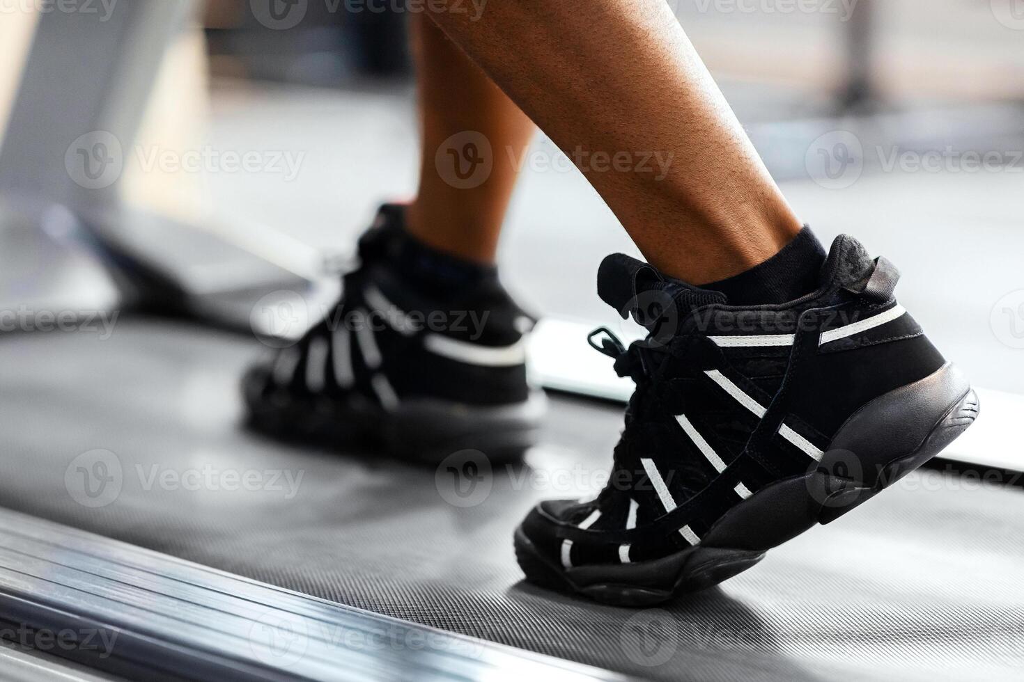 Sports shoes for gym concept. Closeup of unrecognizable african american man bodybuilder walking by treadmill, wearing black and white sneakers, selective focus on shoes, gym interior, copy space photo