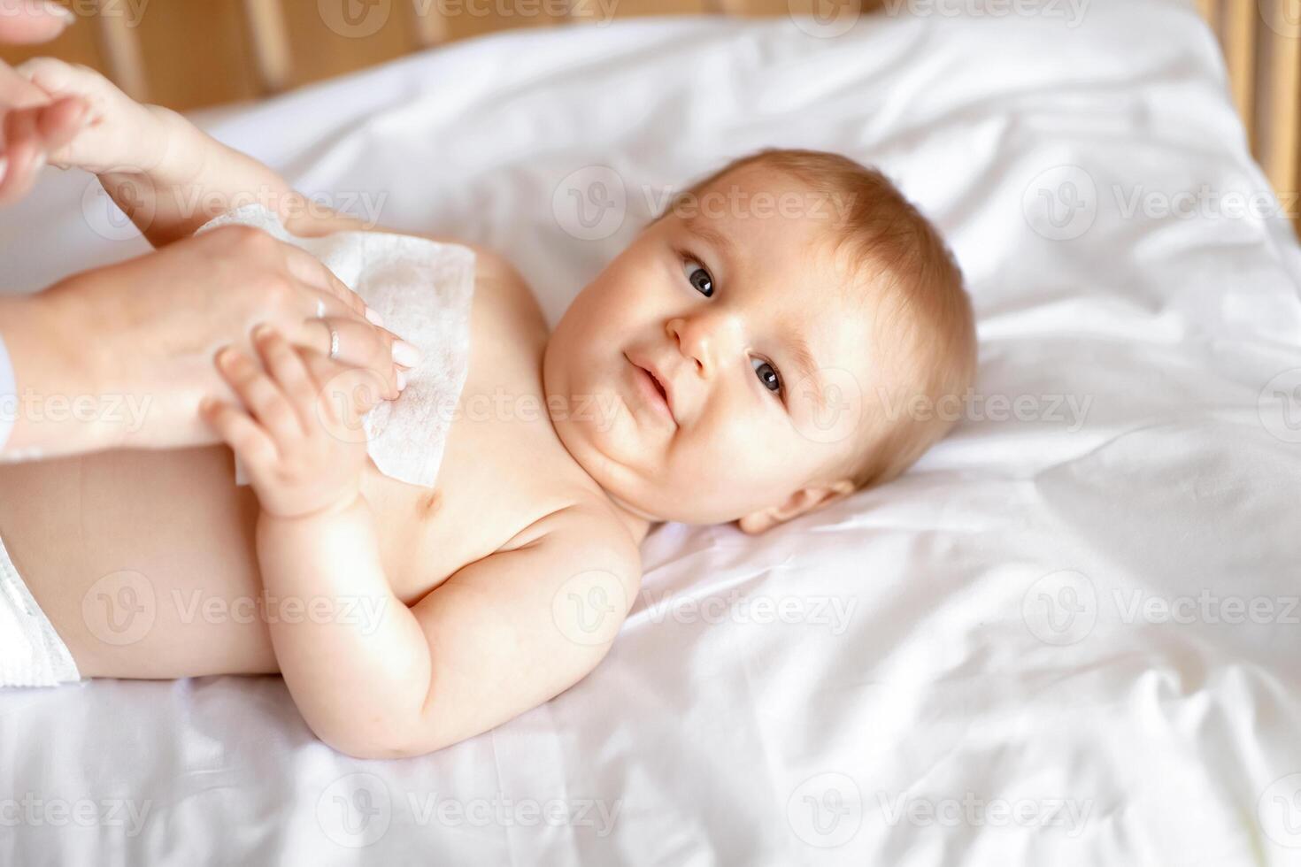 Baby hygiene concept. Unrecognizable mother cleaning cute caucasian toddler body with wet towel, closeup. Adorable baby boy looking at camera while his mom cleaning his belly with wet tissue photo