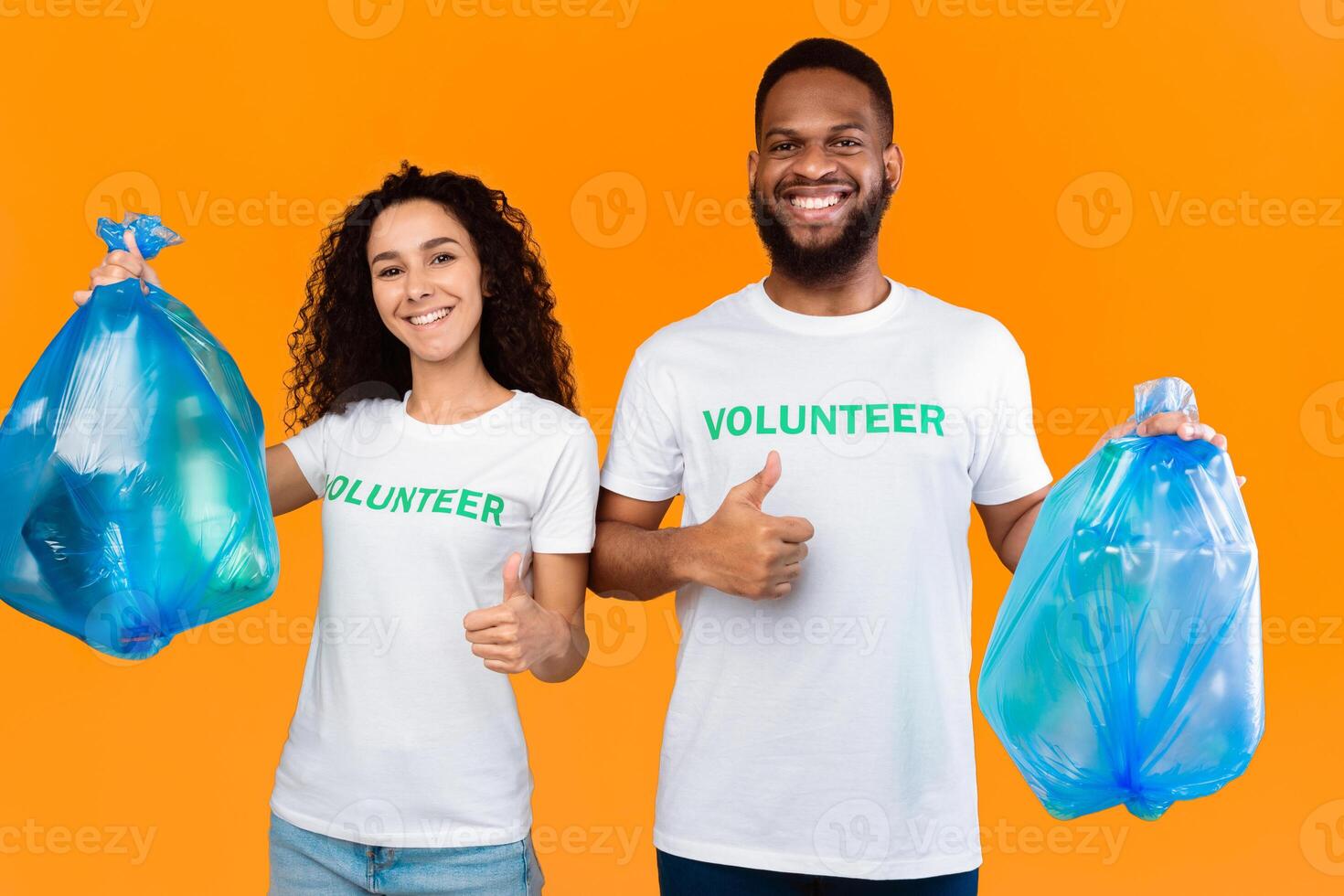 Couple Of Multiethnic Volunteers Holding Blue Plastic Garbage Bags Picking Litter Gesturing Like Standing Over Yellow Studio Background. Volunteering Work, Let's Keep Planet Environment Clean Concept photo