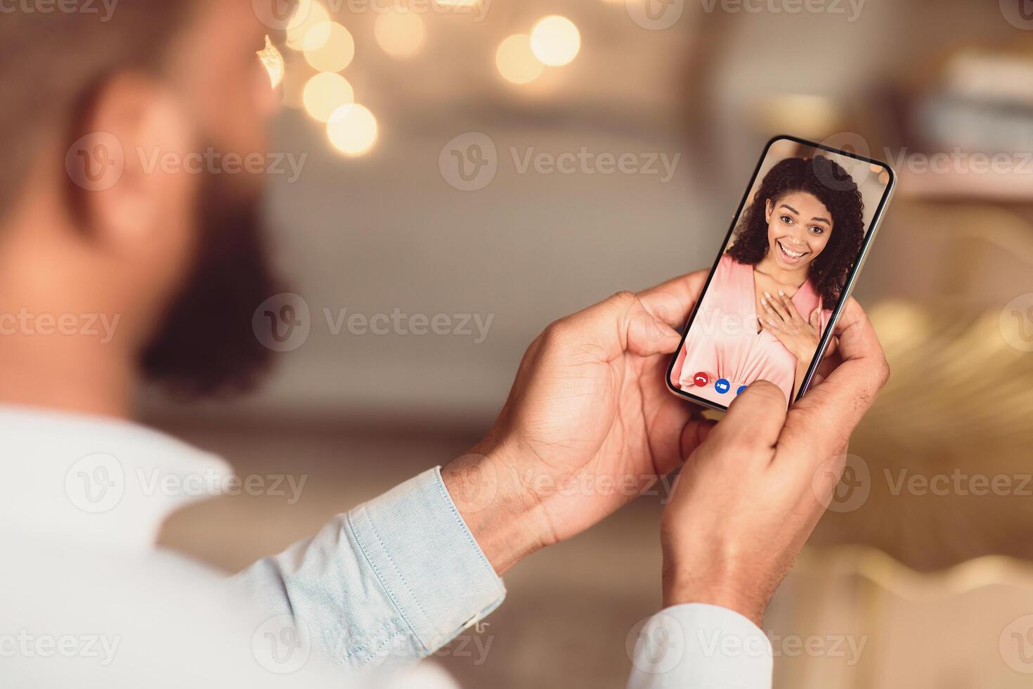 Long Distance Relationship. Back over the shoulder view of black man having online virtual date with his surprised girlfriend, holding and using smartphone app for videochat. Remote Dating photo