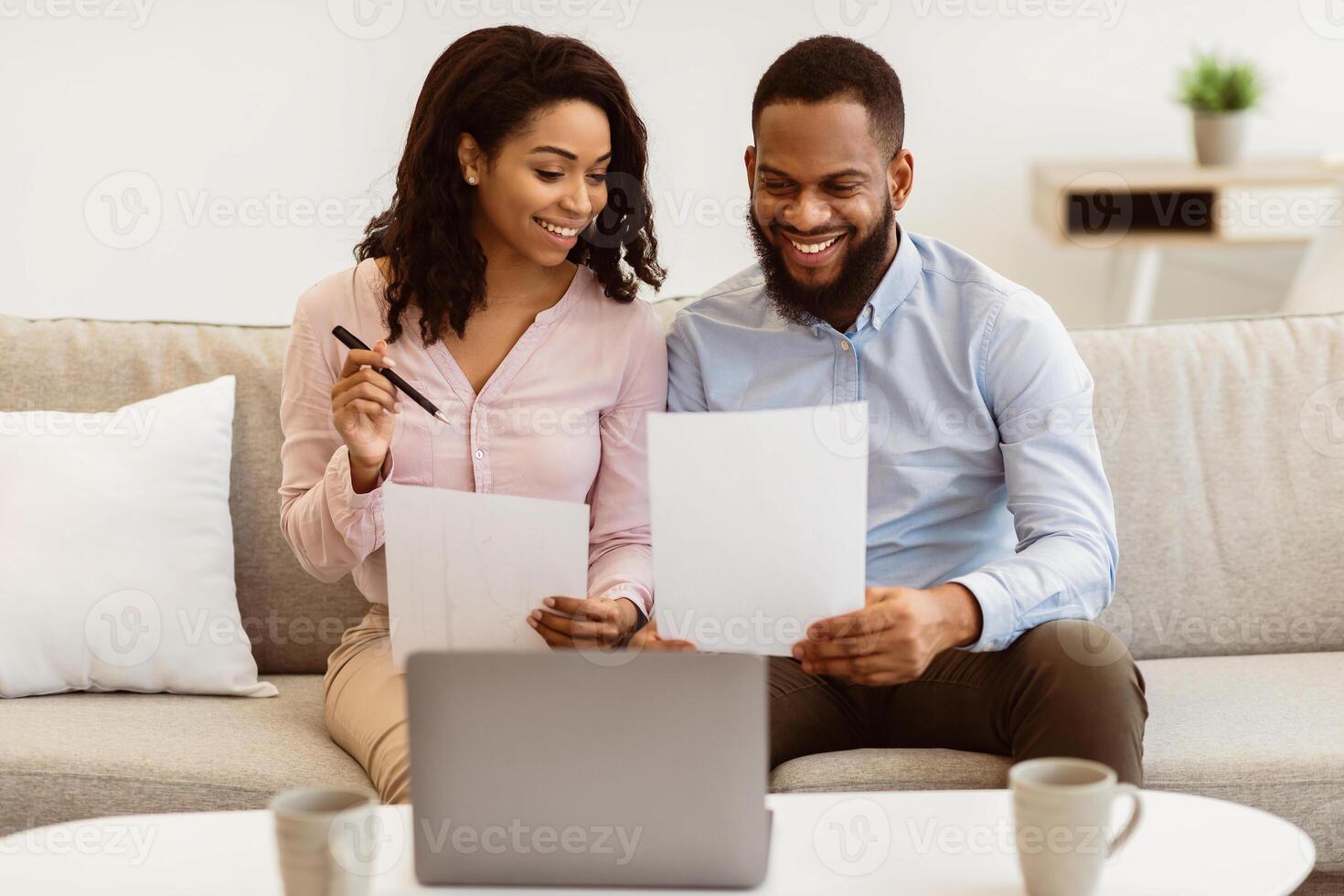 Planning Family Budget. Smiling black couple holding papers, calculating domestic bills and checking household expenses, reading documents or receipt from bank, talking about investment and finance photo