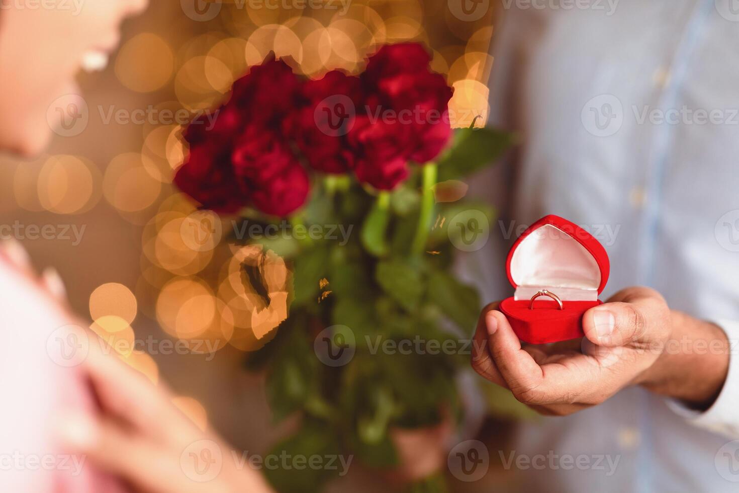 Will You Marry Me. Closeup of unrecognozable african american man showing open box, offering marriage ring to his happy fiance, getting engaged during romantic date, holding bouquet of red roses photo
