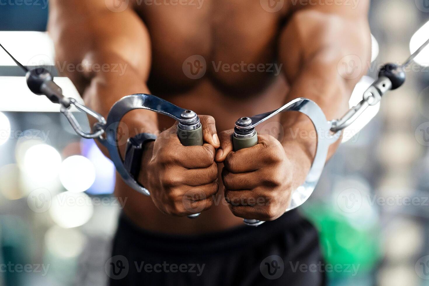 Unrecognizable black man bodybuilder training triceps on crossover exerciser in gym, cropped. Shirtless african american sportsman having workoout at modern gym, closeup. Bodybuilding concept photo