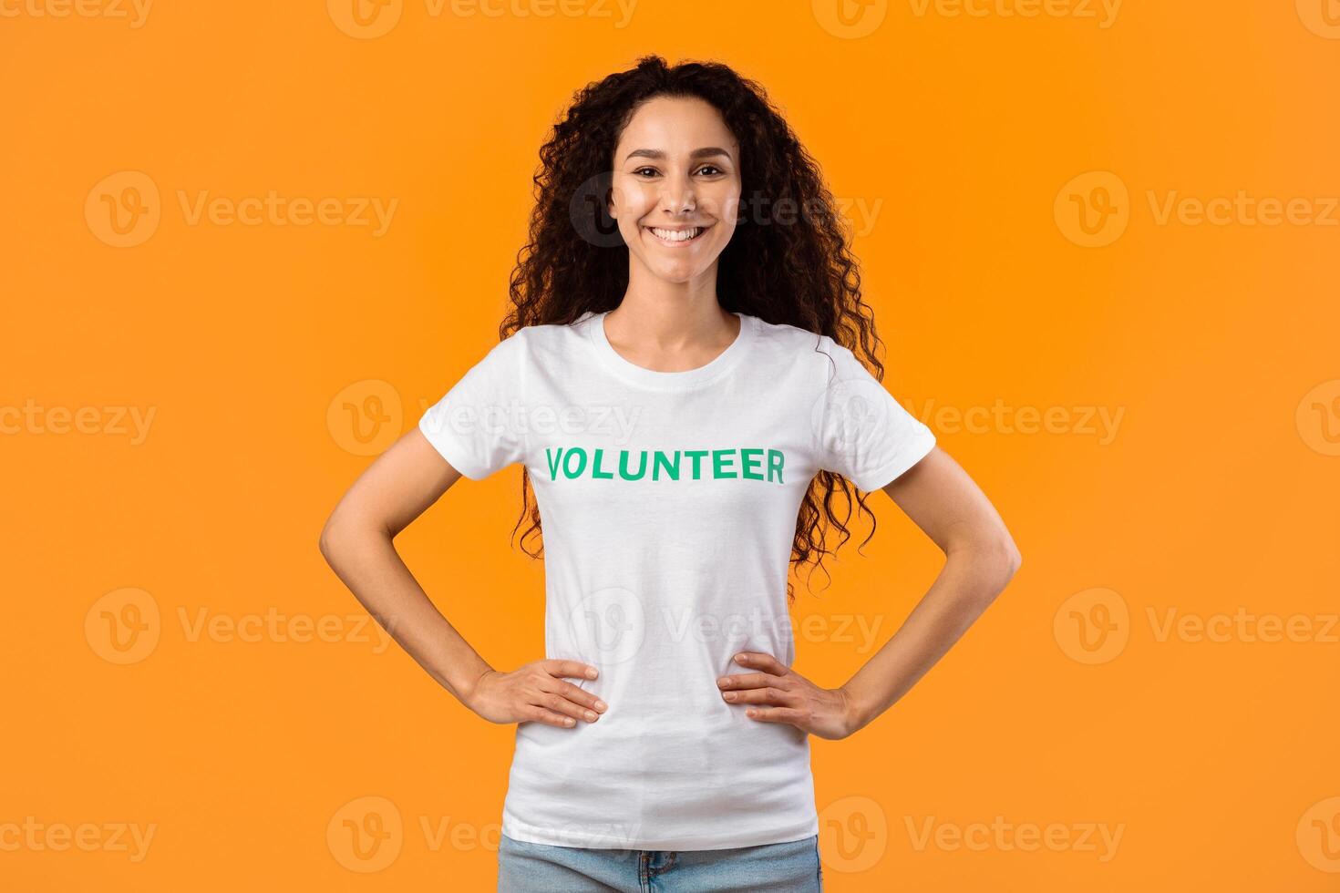 Enthusiastic Volunteer Woman Posing With Hands On Her Hips Smiling To Camera Standing Ready For Voluntary Work Over Yellow Studio Background. Female Activist Portrait. Volunteering Occupation Concept photo