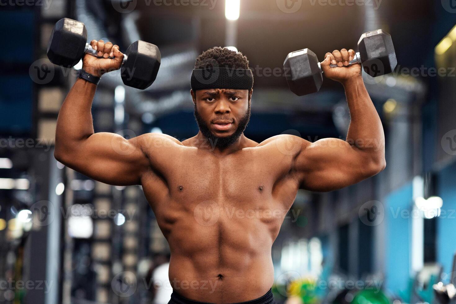 Motivated african american man bodybuilder working on biceps, weight exercises concept. Muscular black guy doing workout with dumbbells at gym, lifting weight up with both hands photo