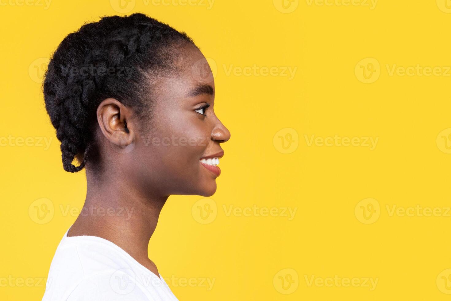 Profile Portrait Of African American Young Woman Smiling Looking Aside At Copy Space Posing Over Yellow Studio Background. Side View, Advertisement With Happy Black Female And Blank Space For Text photo