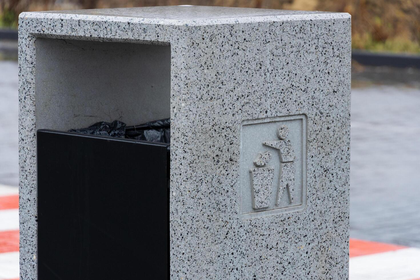 A modern grey garbage container stands in an urban area, inviting passersby to dispose of their trash responsibly. The design promotes recycling and environmental awareness through simple signage photo