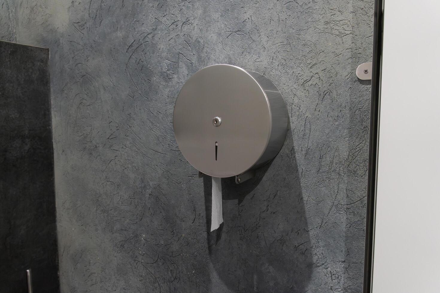 A modern restroom features a round silver paper dispenser affixed to a blue textured wall. This practical fixture is designed for easy access and convenience for users photo