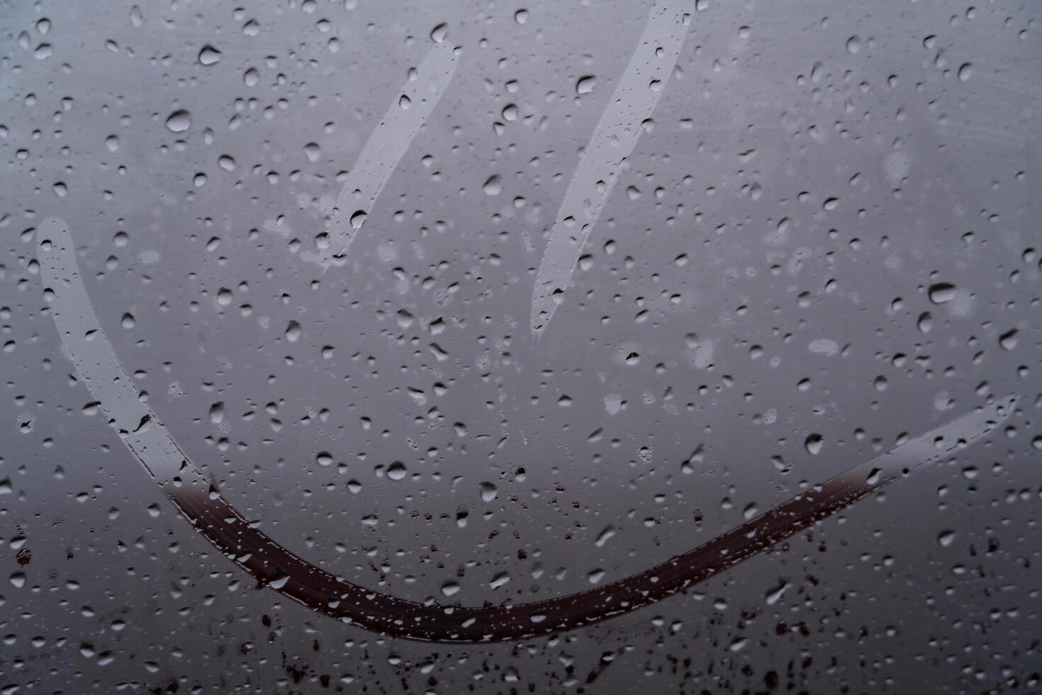 Raindrops softly cascade down a foggy window, creating a serene atmosphere. A playful smiley face drawn through the mist brings a sense of warmth and joy to an otherwise dreary day photo