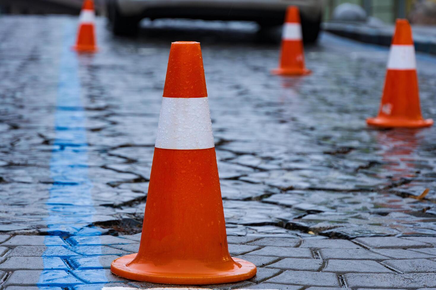 Colorful traffic cones provide clear direction on a wet and glossy street. Rain droplets enhance the environment, reflecting colors and creating patterns on cobblestones photo