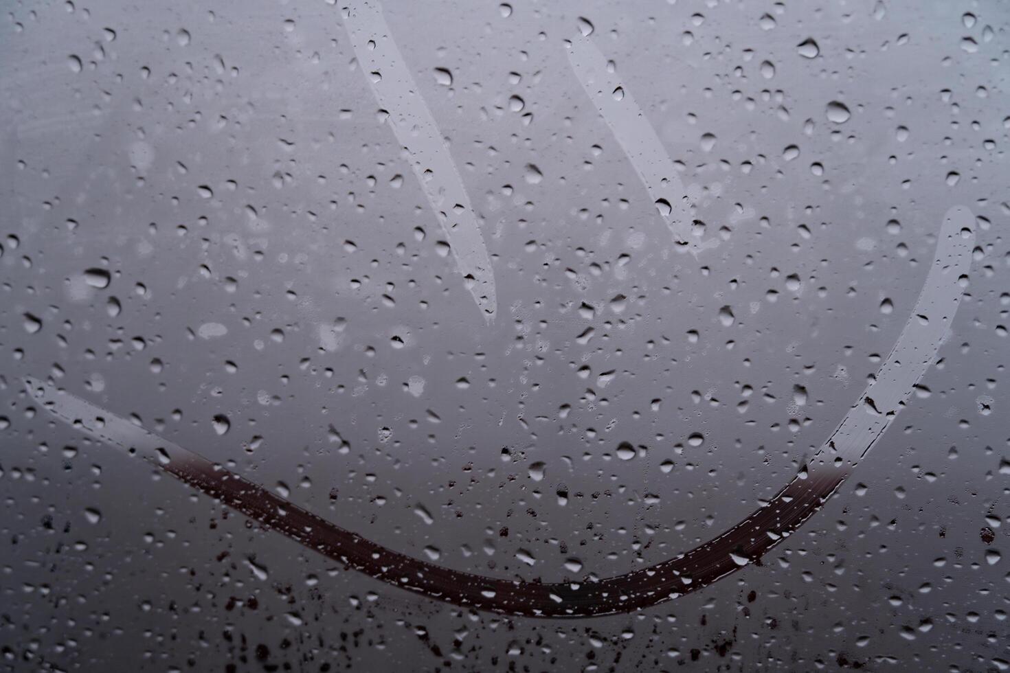 Delicate raindrops cling to a glass surface, blurring the world outside. A joyful smile traced through the mist captures the whimsy of a dreary day, enhancing the cozy atmosphere inside the vehicle photo