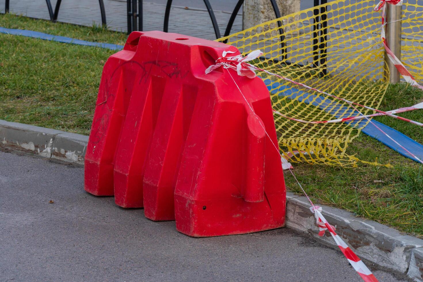 A striking red barrier stands guard on a city street, surrounded by yellow construction netting. Caution tape flutters gently in the breeze, alerting pedestrians to the ongoing work nearby photo