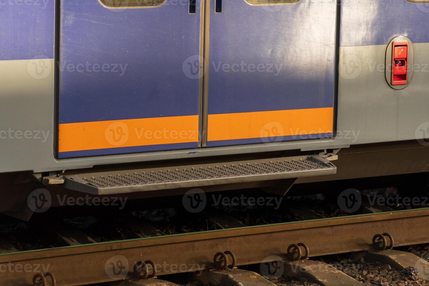 Brightly colored electric train doors stand open, ready for passengers at a bustling railway station. The morning sun casts soft shadows on the platform, inviting commuters to board photo