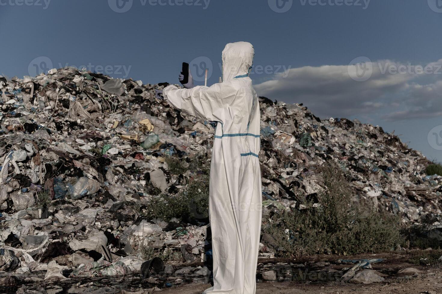 A person dressed in protective gear surveys a sprawling landfill, capturing the overwhelming sight of plastic waste and debris affecting the ecosystem under a clear sky photo