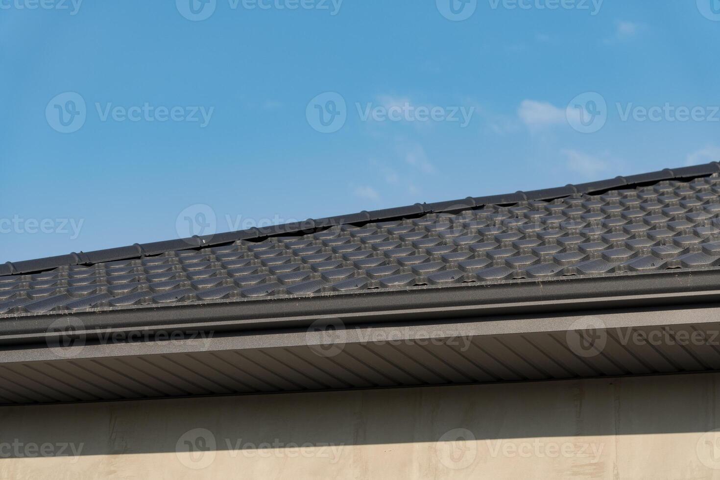 A close-up view of a contemporary residential rooftop is captured under a vibrant blue sky. The sleek metallic tiles reflect sunlight, accentuating the modern architectural design of the home photo