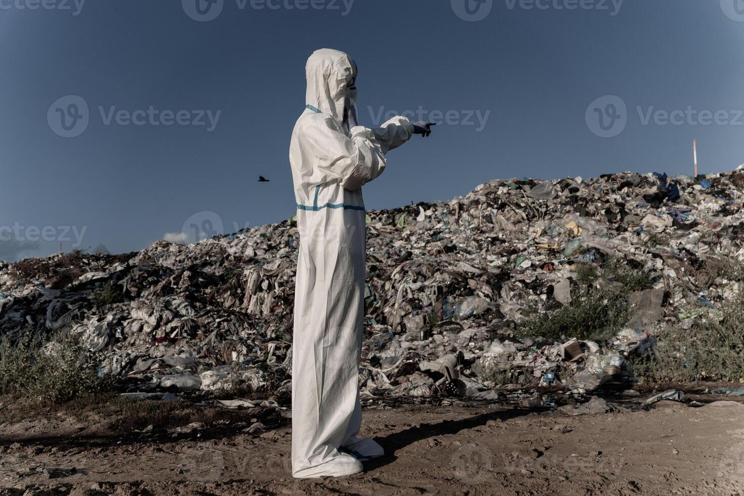 A figure dressed in protective gear surveys a sprawling landfill, highlighting the extensive impact of pollution on the ecosystem and the urgent need for better waste management practices photo