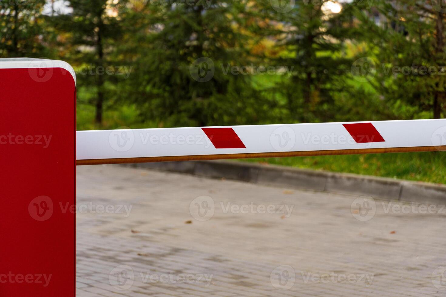 An automatic barrier gate stands closed, effectively controlling entry into a parking lot. The red and white design complements the lush greenery, ensuring safety and organization photo