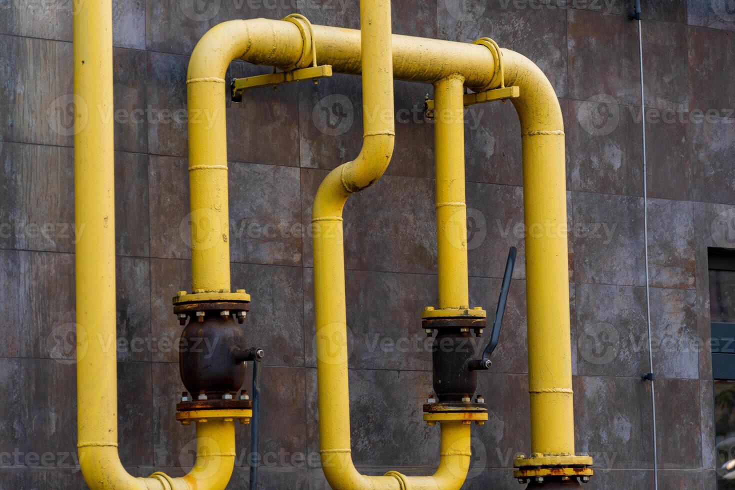 Bright yellow gas pipes wind along a concrete wall, showcasing the intricate connections of energy transportation. Industrial components hint at a complex infrastructure that powers cities photo