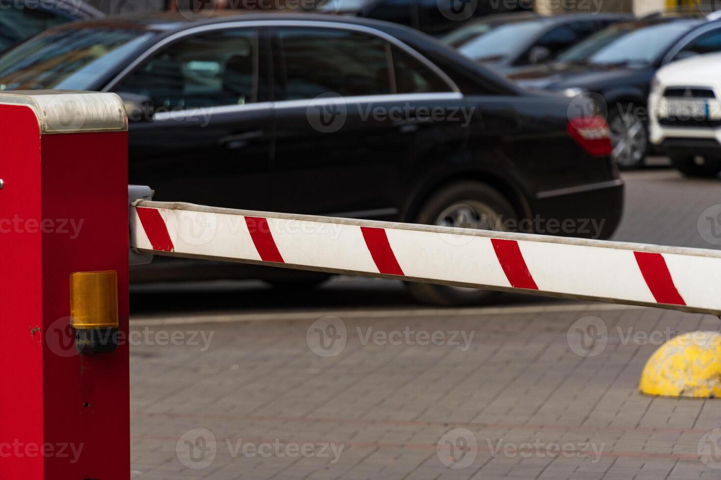 A bright red barrier stands at the entrance of a busy parking lot, preventing entry while vehicles wait in line. The scene reflects measures for safety and security in public spaces photo