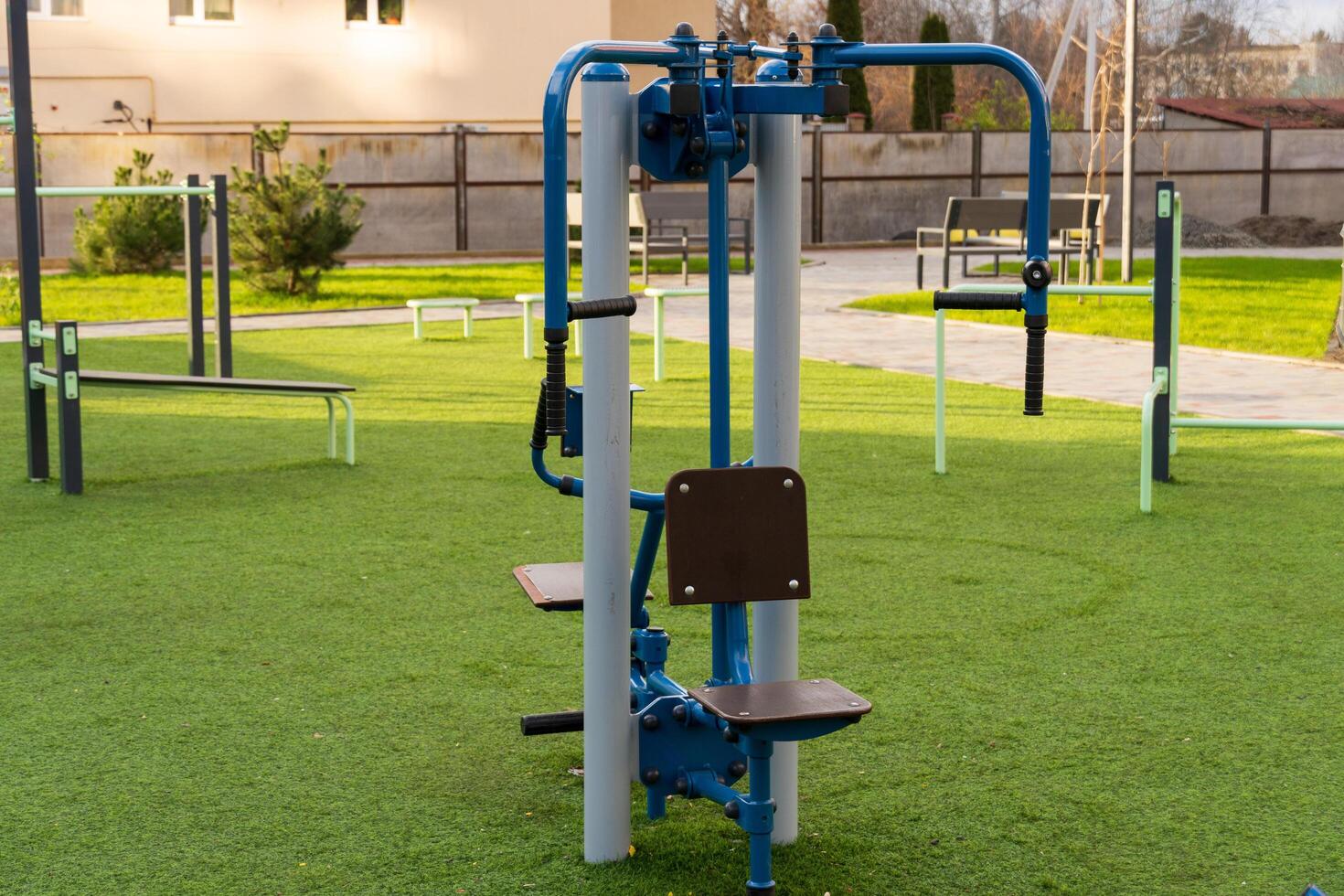 A piece of fitness training equipment stands ready for use in an outdoor gym, surrounded by green grass and other exercise areas, providing a healthy lifestyle option for the community photo