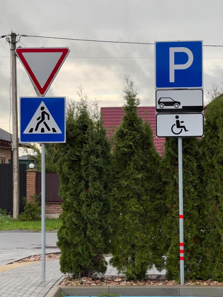 Several road signs stand at an intersection, displaying a pedestrian work zone symbol and designated parking for vehicles and handicapped access. The setting reveals nearby greenery and urban scenery photo