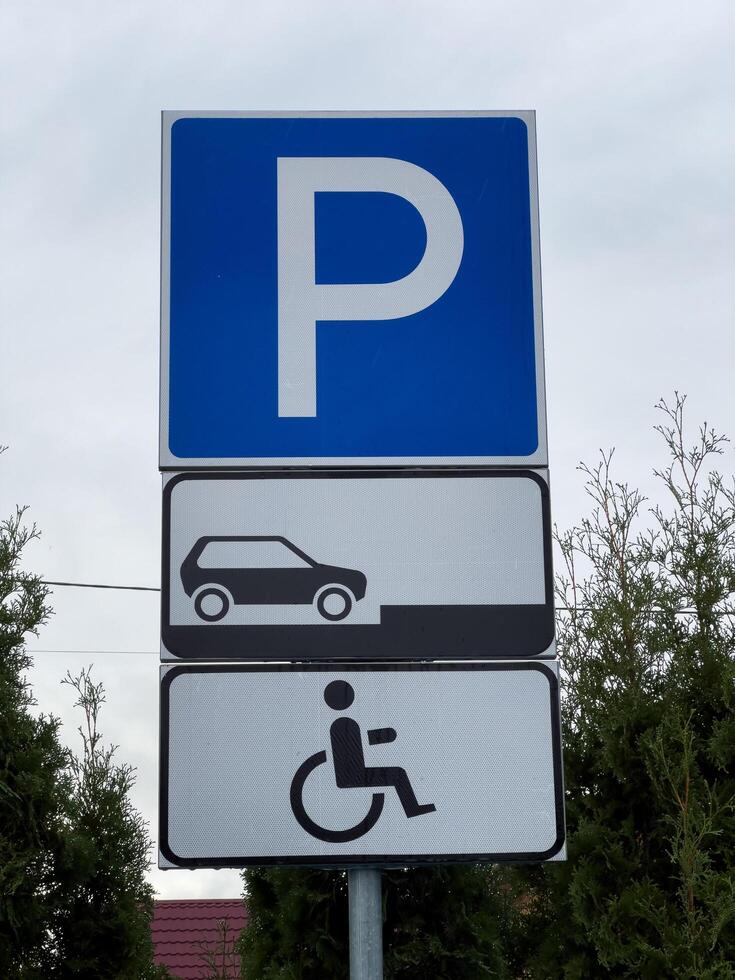 A clear parking sign stands between green shrubs, displaying a designated area for vehicles and additional space for accessible parking. It is important for guiding drivers in a busy area photo
