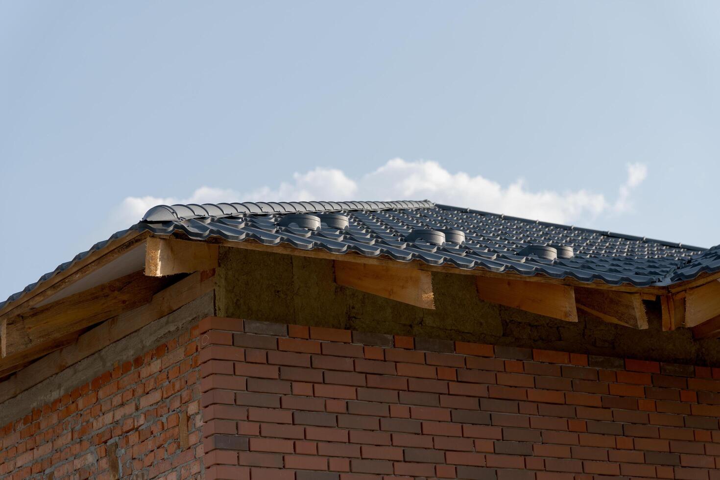 A detailed view of a modern residential rooftop showcases metallic tiles expertly arranged on a brick structure. The clear blue sky enhances the architectural design and construction details photo
