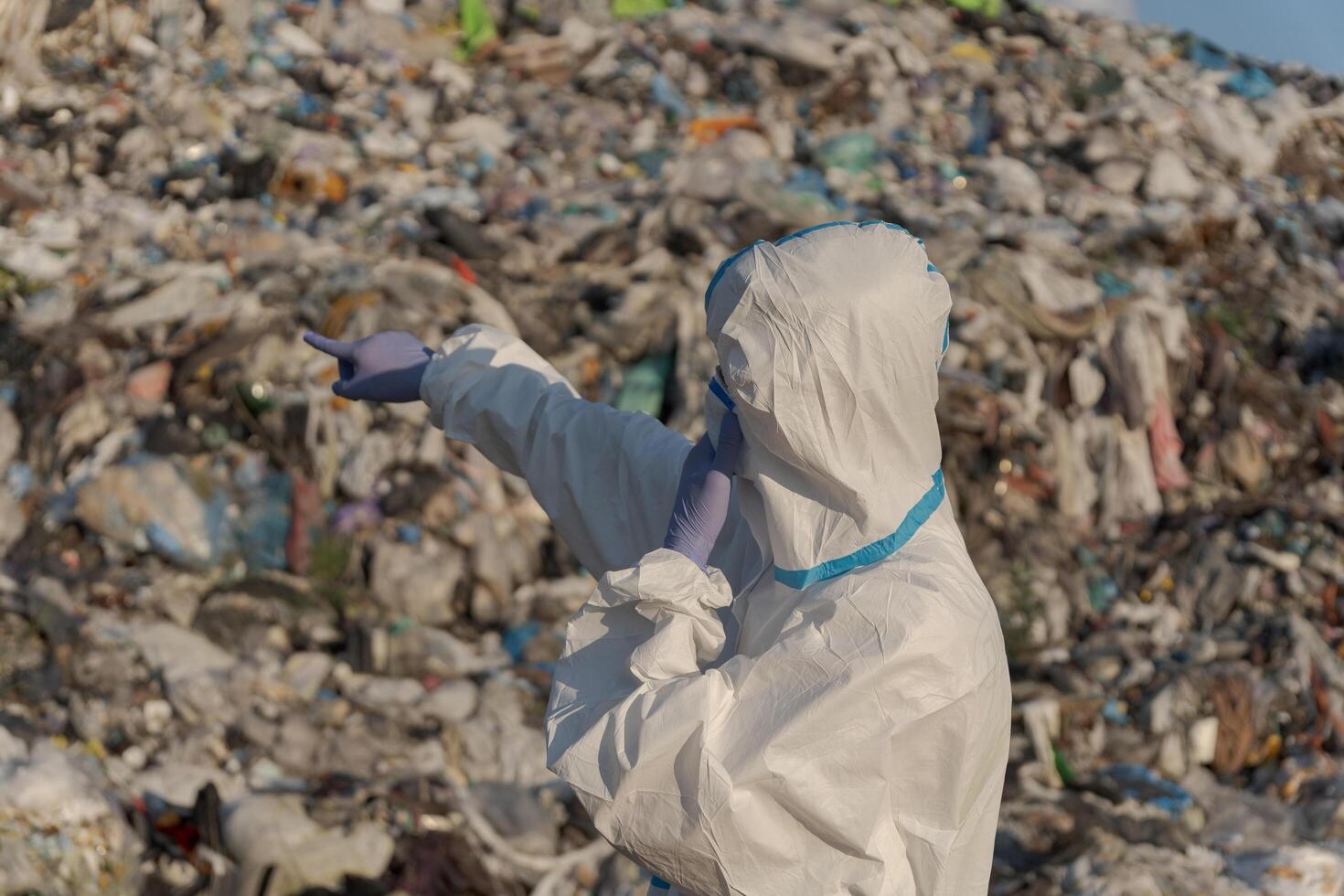 A sanitation worker in protective gear points at a towering mountain of trash at a landfill, highlighting the urgent need for waste management and recycling amid rising pollution concerns photo