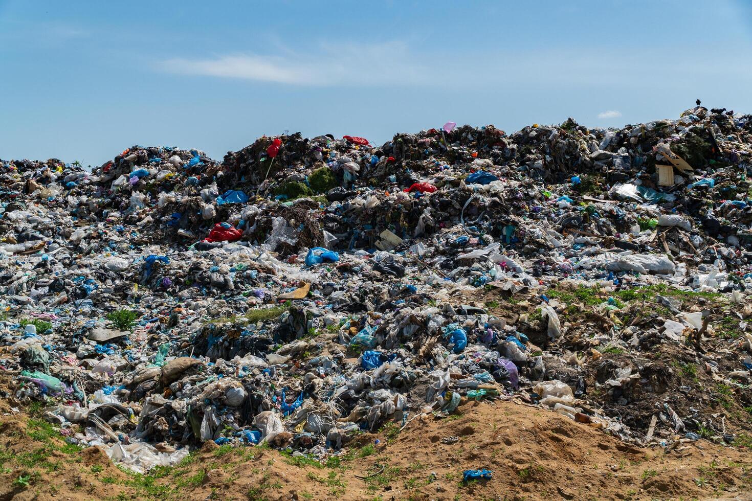 A vast landfill filled with mounds of plastic waste and debris under a clear blue sky. The site illustrates the significant impact of pollution on the surrounding ecosystem and sanitation efforts photo